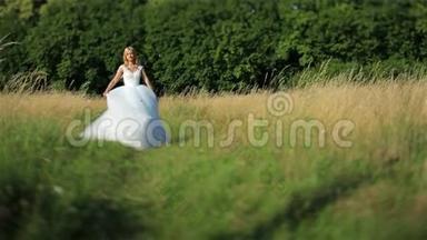 美丽浪漫时尚的金发新娘，穿着白色连衣裙，在阳光下在绿色的田野里跳舞